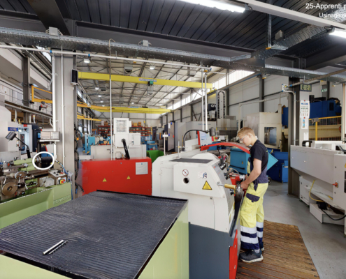 L’image montre un apprenti polymécanicien travaillant sur une machine-outil dans un atelier mécanique bien équipé.