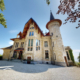 Cette image montre la façade extérieure d'une grande villa (château) avec vue sur le lac. Cette photo est prise depuis le jardin et donne sur l'entrée de la villa.